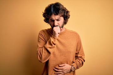 Young handsome man with beard wearing casual sweater standing over yellow background feeling unwell and coughing as symptom for cold or bronchitis. Health care concept.