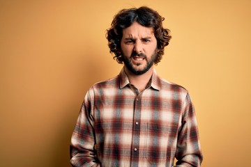 Young handsome man with beard wearing casual shirt standing over yellow background skeptic and nervous, frowning upset because of problem. Negative person.