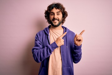 Young handsome sporty man with beard wearing casual sweatshirt over pink background smiling and looking at the camera pointing with two hands and fingers to the side.