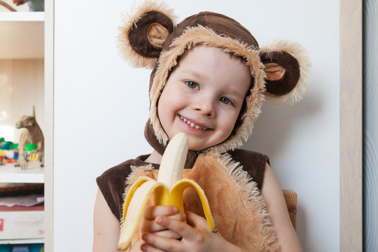 Image of cute toddler wearing a monkey costume, eating a banana