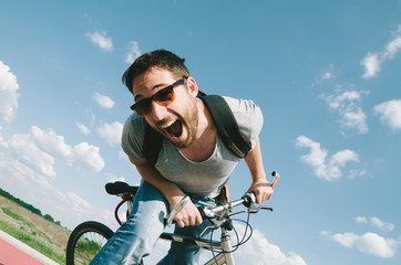 Happy cool hipster guy with bicycle having fun. Summer bike travel adventure in nature. Sexy positive man with excited face cycling on road trip in countryside.