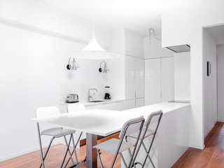 New stylish bright kitchen with white cabinets. Spacious modern interior with wooden floor, white table, industrial chairs and big ceiling window.