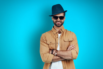 Good looking young man smiling and looking at camera while standing against blue background