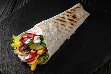 A delicious doner donair kebab wrap with meat, lettuce, tomato, red onion and sauce.