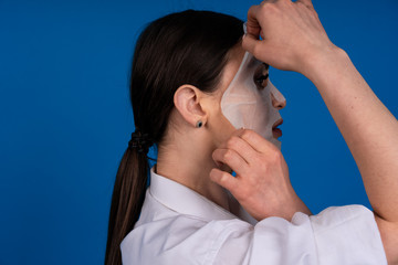 The profile of a girl with her hair gathered in a ponytail, she's a nice gesture removes tissue mask, concept skin care face