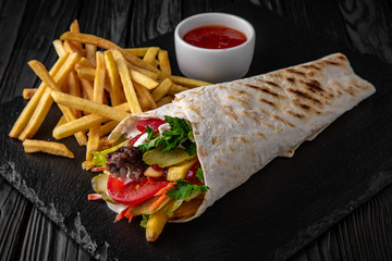 A delicious doner donair kebab wrap with meat, lettuce, tomato, red onion and sauce with french fries and sauce.
