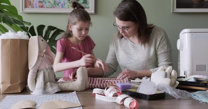 Happy mother and daughter sewing together toy bunny doll at home