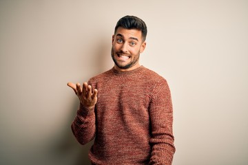 Young handsome man wearing casual sweater standing over isolated white background smiling cheerful with open arms as friendly welcome, positive and confident greetings