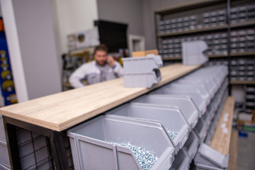 Focus on white metal screws in a plastic box. Behind is a man talking on the phone. Screws in a hardware store and building supplies.