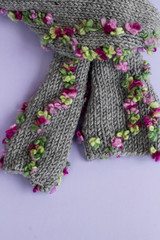 Hand knitted womens stylish gray scarf with beautiful flower motif on pastel background.
