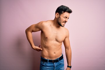 Young handsome strong man with beard shirtless standing over isolated pink background Suffering of backache, touching back with hand, muscular pain