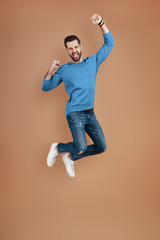 Full length of cheerful young man smiling and gesturing while hovering against brown background