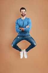 Fototapeta na wymiar Full length of happy young man smiling and keeping arms crossed while hovering against brown background