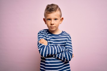 Young little caucasian kid with blue eyes wearing nautical striped shirt over pink background skeptic and nervous, disapproving expression on face with crossed arms. Negative person.
