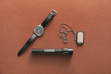 Modern flashlight with tag and watch on color background