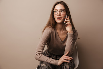Photo of pleased woman talking on cellphone and sitting on chair