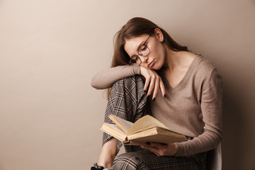 Photo of charming sad woman reading book and sitting on chair