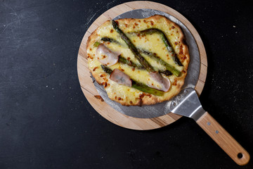 selbstgemachte Pizza mit Mascarpone, Mozzarella, Sauce hollandaise, grünem Spargel, Truthanschinken auf einer Seite, Studio