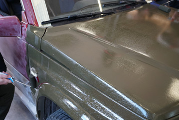 close up of a man painting an old jeep in army green with a paintbrush and paint