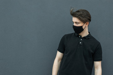 Portrait of guy in black t-shirt and black medical mask on his face on dark gray background for protect and stop viruses and coronavirus pandemic, covid-19 outbreak