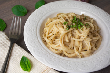 A vegan version of traditional Italian pasta fettuccine alfredo with creamy white sauce garnished with basil on a wooden surface with a fork, napkin, garlic and basil leaves