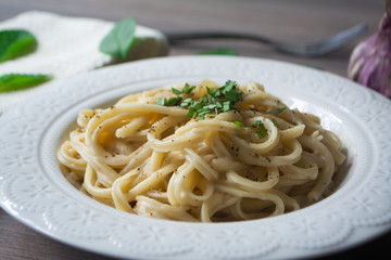 A vegan version of traditional Italian pasta fettuccine alfredo with creamy white sauce garnished with basil on a wooden surface with a fork, napkin, garlic and basil leaves