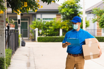 Asian young delivery man courier hold parcel post boxes he protective face mask service and walk looking for customer home location, under curfew pandemic coronavirus COVID-19