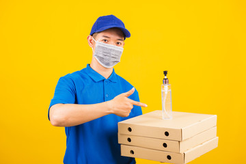 Fototapeta na wymiar Asian young handsome delivery man wearing face mask protective germ virus holding boxes on hand and point alcohol sanitizing gel, studio shot isolated yellow background, outbreak coronavirus COVID-19
