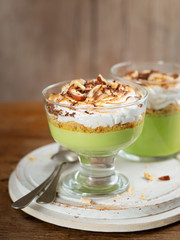Matcha green tea panna cotta with coconut milk topped with hazelnut and burnt meringue on a wooden background in glasses. Concept healthy gluten-free dessert for summer. Selective focus. Copy space.