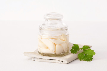 fermented garlic in a closed transparent jar on a white table. Decorated with cilantro