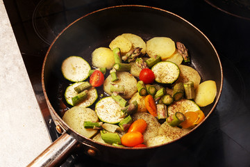  Pfanne auf einer Herdplatte mit Kartoffeln, Zucchini, kleine Strauchtomaten und grünen Spargel.