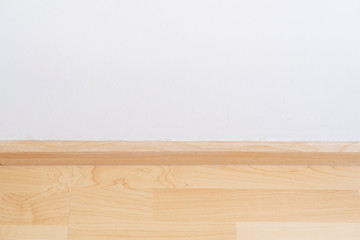Wooden wall base skirting, finishing material with wood laminate floor and white mortar wall.