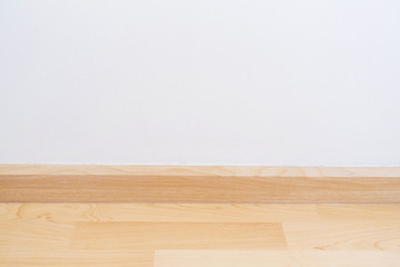 Wooden wall base skirting, finishing material with wood laminate floor and white mortar wall.