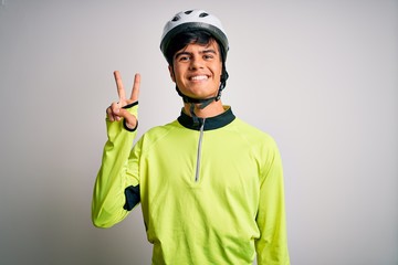 Young handsome cyclist man wearing security bike helmet over isolated white background smiling with happy face winking at the camera doing victory sign. Number two.