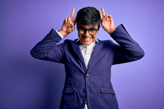 Young handsome business man wearing jacket and glasses over isolated purple background Posing funny and crazy with fingers on head as bunny ears, smiling cheerful