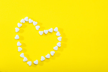 Heart-shaped tablets on a yellow background. Flat bed, top view.