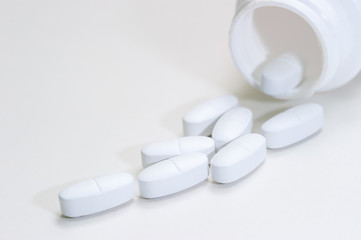 Tablets are poured out of the jar on a white background. Vitamins, medications, front view.