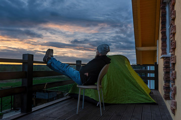 Wanderlust at the coronavirus quarantine. Man sitting by the tent admires the sunset from the terrace.