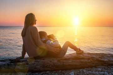 Fototapeta na wymiar Mother and son tourist traveling sitting on the beach and look binocular under sunset sky with sun in summer. Mothers Day. 