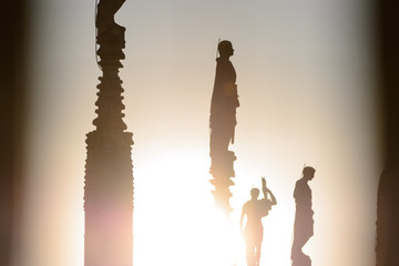 Milano, Italy, march 22, 2019: on the roof top of the Duomo church silhouettes backlit of some of the many statues on top of the spiers of this magnificent church at sunset time