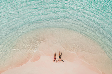 Couple lying on famous pink beach in Komodo national park. Turquoise mint color clear water, tropical vacations on honeymoon. Drone aerial view from above. - 347853533