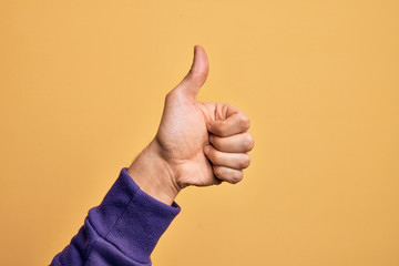 Hand of caucasian young man showing fingers over isolated yellow background doing successful approval gesture with thumbs up, validation and positive symbol - obrazy, fototapety, plakaty
