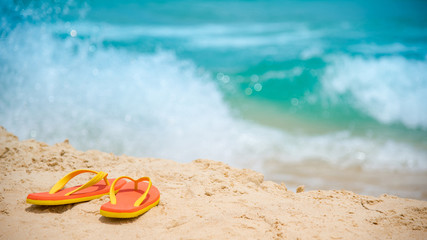 Orange flip flops or slippers on tropical island beach. Footwear for summer holiday or relaxing vacation. Summertime travel concept