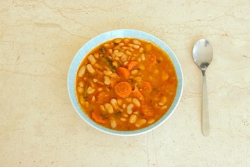 Red bean soup with beans, carrots, and tomato sauce on a plate isolated on a marble table with a spoon