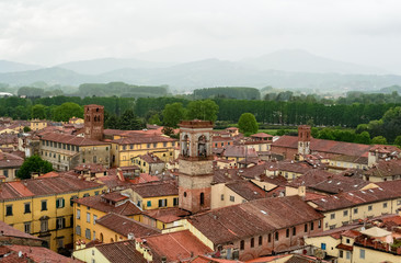 Fototapeta na wymiar From the Guinigi's tower a landscape aerial view of the typical italian red roofs of the medieval town of Lucca in Tuscany, Italy during a rainy winter day 