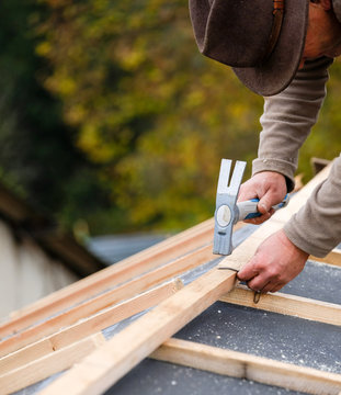 construction worker on a renovation roof covering it with tiles using hammer, crane and grinder
