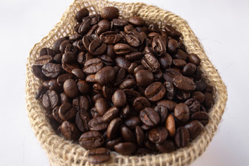 Roasted coffee beans in jute bag on white background