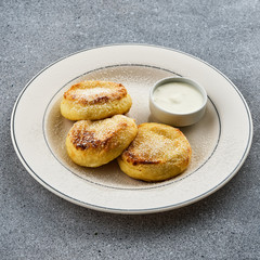 Cheesecakes with sour cream, sprinkle with powdered sugar on a white plate