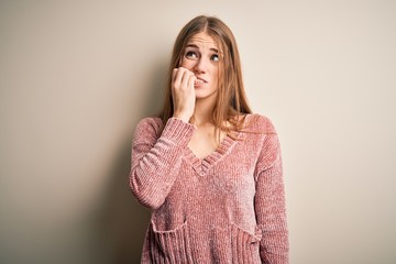 Young beautiful redhead woman wearing pink casual sweater over isolated white background looking stressed and nervous with hands on mouth biting nails. Anxiety problem.