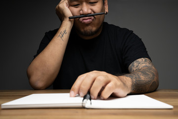 Asian man writing on a note book with thinking face on wooden table. Concept about work remotely.